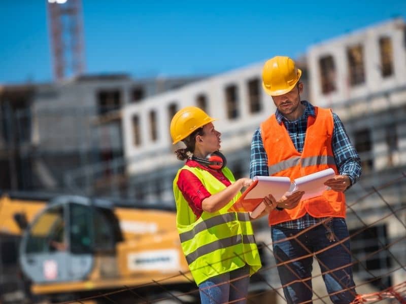 Construction survey professionals reviewing development plans at an active urban construction site before layout and staking work.